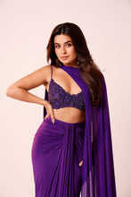 Load image into Gallery viewer, A woman modeling a purple draped outfit with a beaded crop top and a flowing sheer cape against a plain light beige studio background.