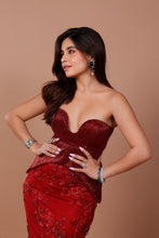 Load image into Gallery viewer, A woman posing in a strapless, deep red sequined gown with floral lace detailing on the skirt, set against a solid warm brown studio background.