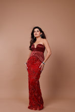 Load image into Gallery viewer, A woman modeling a strapless red evening gown with a deep V-neckline and a fitted silhouette, standing against a solid warm beige studio backdrop.