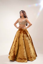 Load image into Gallery viewer, A woman modeling a traditional Indian outfit featuring a metallic gold flared skirt and a matching beige embroidered crop top, set against a plain light background with a lens flare.