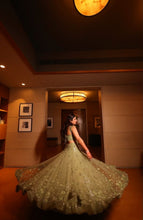 Load image into Gallery viewer, A woman wearing a voluminous embellished green gown twirls in a warmly lit indoor space, holding out the wide skirt to show its full span.
