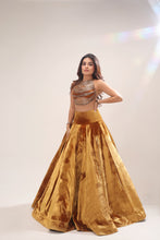 Load image into Gallery viewer, A woman modeling a traditional Indian outfit consisting of a metallic gold and bronze embellished crop top and a voluminous gold velvet skirt, set against a plain light beige studio background.
