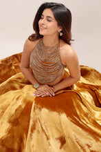 Load image into Gallery viewer, A woman wearing a luxurious metallic gold velvet ball gown with a heavily embellished beaded halter top, seated against a neutral beige background.
