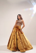 Load image into Gallery viewer, A woman modeling a luxurious mustard-gold velvet two-piece outfit, featuring a high-waisted flared skirt and a matching ruched crop top, set against a neutral studio backdrop with a bright lens flare.
