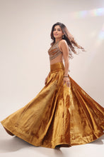 Load image into Gallery viewer, A woman modeling a traditional Indian outfit consisting of a metallic gold flared skirt and a matching embellished crop top, set against a plain light beige studio background.

