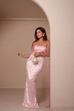 Load image into Gallery viewer, A woman models a light pink evening gown with a sheer mesh overlay draped over her shoulders, standing in a minimalist beige room with an arched doorway.
