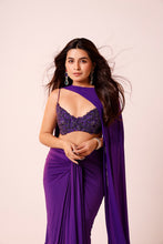 Load image into Gallery viewer, A woman modeling a purple traditional outfit consisting of a sleeveless embroidered crop top and a draped skirt with a long matching scarf, against a solid pale pink background.
