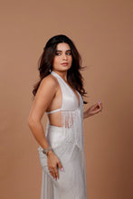 Load image into Gallery viewer, A woman modeling a white sleeveless halter dress with fringe detailing and a textured, shimmering fabric, posed against a solid warm brown studio backdrop.
