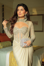 Load image into Gallery viewer, A woman wearing a beige and silver embellished sari with a sheer embroidered bustier bodice, holding a silver clutch in a warmly lit indoor setting.
