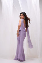 Load image into Gallery viewer, A woman modeling a lavender purple sleeveless maxi dress with an open lace-up back, standing in front of a white draped fabric backdrop.
