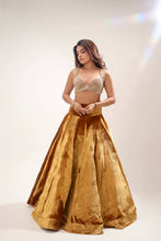 Load image into Gallery viewer, A woman modeling a traditional Indian outfit featuring a voluminous gold skirt and a beige lace bralette, set against a plain light beige studio background with a subtle lens flare.
